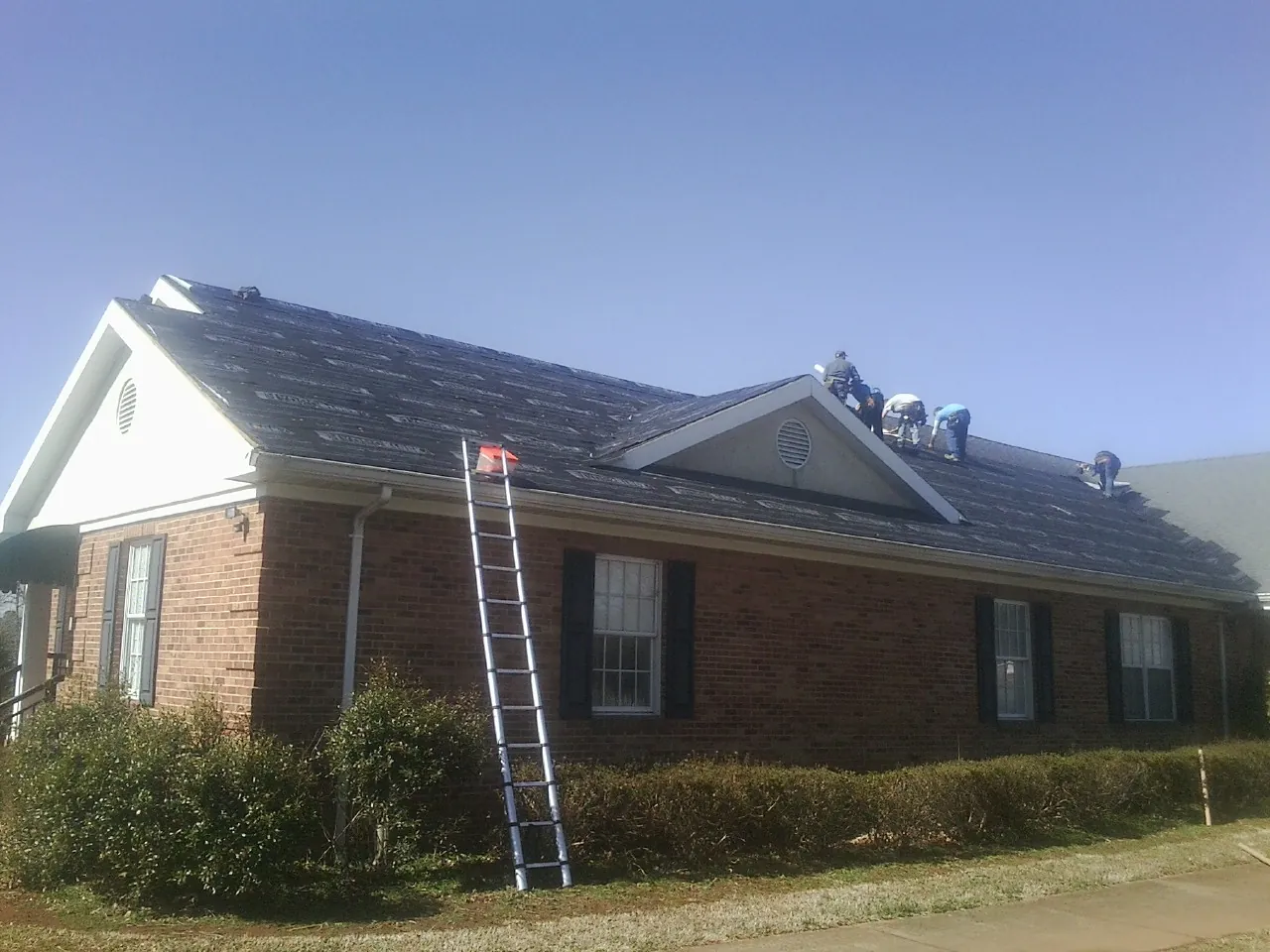 Crew tearing shingles off a brick ranch roof with a ladder set — Emergency Roof Repair work by our crew in Westminster